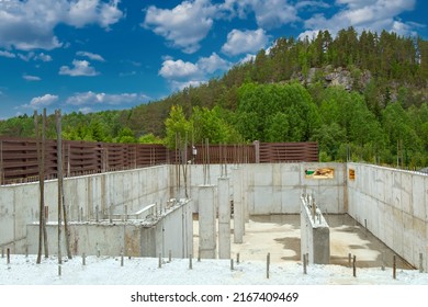 Construction of concrete. Foundation building with columns. Columns and walls made of concrete. Armature sticks out of columns of building. Taiga and hill behind construction building