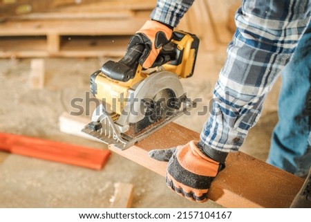 Construction Contractor Cutting To Size Wood Beam Using Portable Circular Saw Close Up Photo. Industrial Equipment Theme.