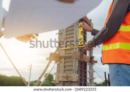 Construction contractor discussing, checking and recording construction work using computer, tape measure, spirit level and wearing yellow construction equipment. House construction concept.