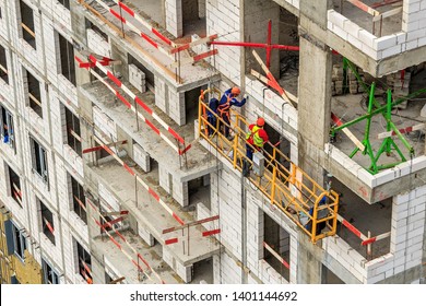 Construction cradle on wall of monolithic house under construction. Electric suspended platform is reliable for working safely at elevated height in accordance, applicable standards. Panoramic windows