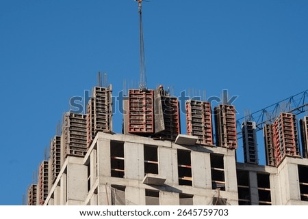 Construction crane lifting formwork during building construction process against a clear blue sky