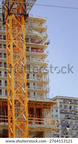 Construction crane next to an incomplete building with scaffolding and clear sky above