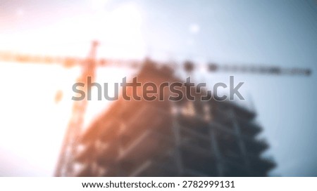 A construction crane is positioned above a building under development, with a bright sky and lens flare.