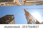 Construction Crane Towering Above Building. A towering yellow construction crane positioned between tall buildings under a bright blue sky.