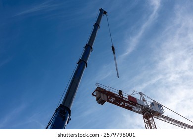 Construction of a construction crane using a mobile crane. Daytime shot of both machines against a blue sky