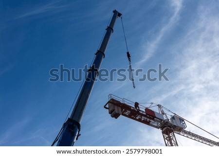 Construction of a construction crane using a mobile crane. Daytime shot of both machines against a blue sky