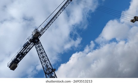 Construction Crane Viewed from Below. Low-angle view of a construction crane against bright blue sky with scattered clouds, emphasizing scale and industrial structure.