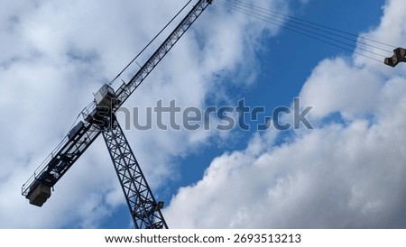 Construction Crane Viewed from Below. Low-angle view of a construction crane against bright blue sky with scattered clouds, emphasizing scale and industrial structure.