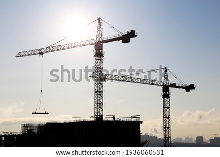 Construction cranes above the unfinished residential building against sunshine. Housing construction, apartment block in city