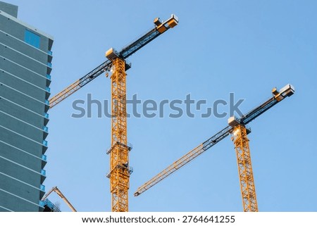 Construction cranes lifting materials for a new skyscraper against a clear blue sky