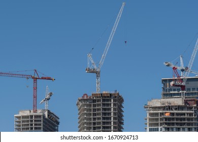 Construction Cranes Next To Modern High Rise Tall Condo And Office Building That Are Being Built. New Housing, City Developments, Real Estate Market Concept.