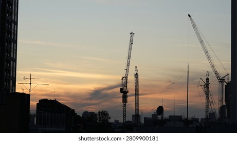 Construction cranes silhouette against dramatic orange sunset sky