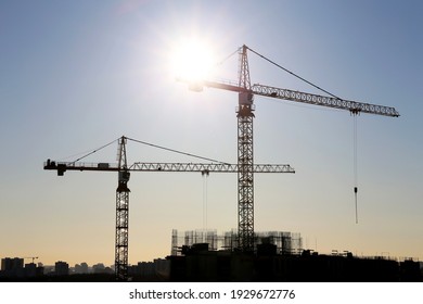 Construction cranes and unfinished residential building on blue sky and sunshine background. Housing construction, apartment block in city - Powered by Shutterstock