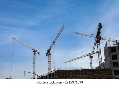 Construction cranes work on creation site against blue sky background. Bottom view of industrial crane. Concept of construction of apartment buildings and renovation of housing. Copy text space - Shutterstock ID 2215371399