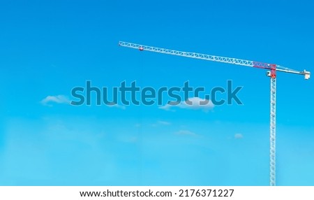 Construction cranes work on creation site against blue sky background. Bottom view of industrial crane. Concept of construction of apartment buildings and renovation of housing. Copy space. 