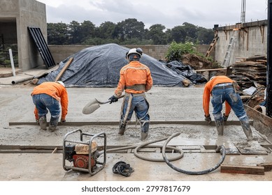 Construction crew using screed board and hand tools to level and finish freshly poured concrete slab during residential building construction