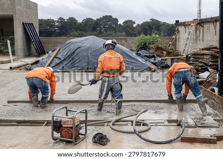 Construction crew using screed board and hand tools to level and finish freshly poured concrete slab during residential building construction