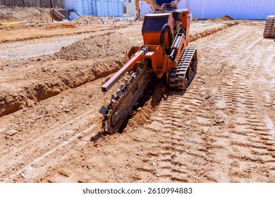 Construction crew utilizes trenching machine to create deep trench for utility lines at building site