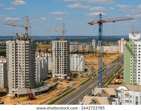 Construction crews work on multiple high-rise residential buildings in a growing city, showing cranes and bustling activity.