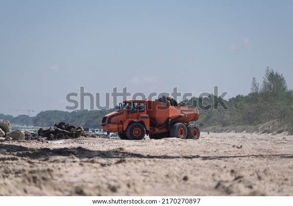 CONSTRUCTION DUMP TRUCK - A big vehicle carries\
boulders on the sea\
beach\
