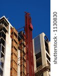A construction elevator rises up the side of a hi-rise being built