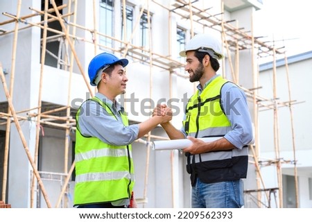 Construction engineer and architect with blueprint shaking hands while standing on construction site. Home building concept