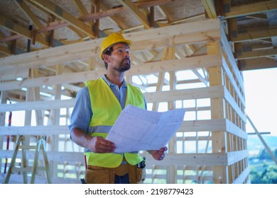 Construction Engineer Or Architect With Blueprints Visiting And Chechking Eco Building Site Of Wood Frame House