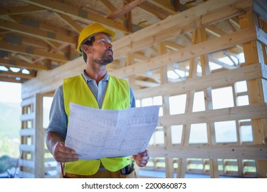 Construction Engineer Or Architect With Blueprints Visiting And Chechking Eco Building Site Of Wood Frame House.