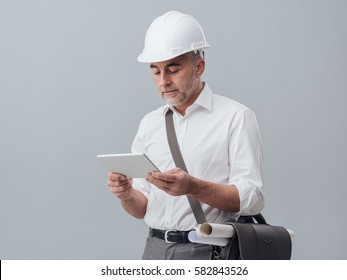 Construction engineer connecting with a digital tablet and using apps, he is wearing a safety helmet