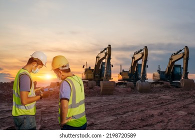 The Construction Engineer And The Foreman Wear Safety Clothing Planning Work With A Tablet Computer To Improve The Construction Site Landscape With 3 Excavators And A Sky In The Background.