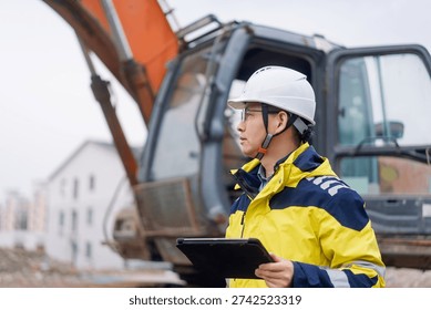 Construction engineer holding tablet while inspecting excavator operation at site