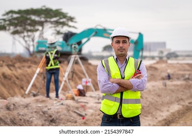 Construction engineer wear safety uniform under inspection and survey workplace by radio communication with excavation truck digging, theodolite and worker construction road background.