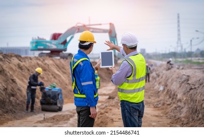 Construction engineer wear safety uniform under inspection and survey workplace by tablet with excavation truck digging and worker construction road background. - Shutterstock ID 2154486741