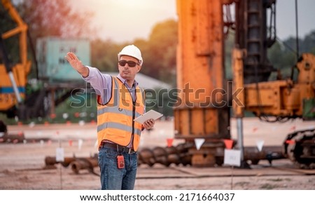 Construction engineer wear safety uniform under inspection and survey workplace by tablet with excavation truck digging, theodolite and worker construction road background.