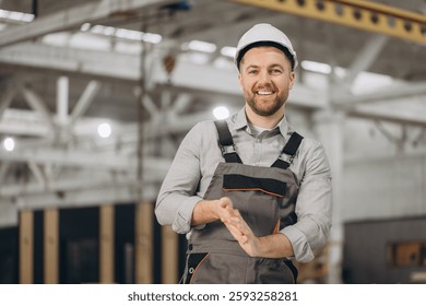 Construction engineer wearing hardhat and work overalls clapping hands inside prefabricated house factory