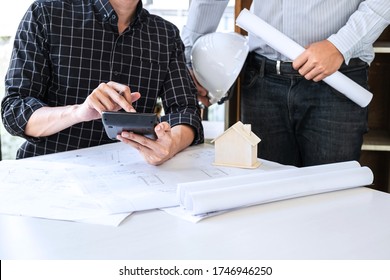 Construction engineering or architect discussing a blueprint and building model while checking information on sketching meeting for architectural project in work site.