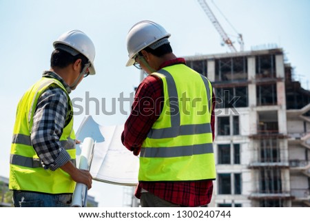 Construction engineers discussion with architects at construction site or building site of highrise building with blueprints.
