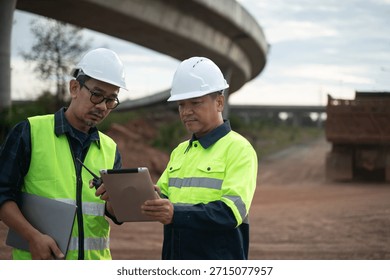 Construction engineers reviewing technical data on tablet with heavy machinery in background, illustrating modern construction technology and progress.
