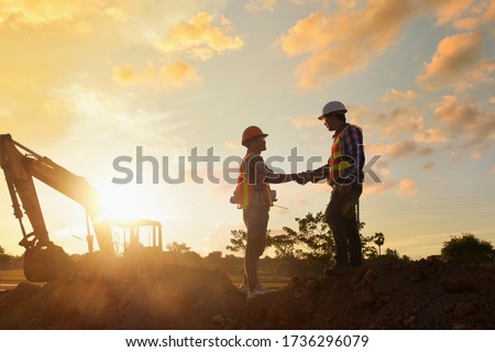 Construction engineers supervising progress of construction project stand on new factory,Engineering Consulting People on construction site holding blueprint in his hand. Building inspector