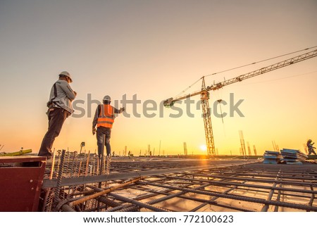 Construction engineers supervising progress of construction project stand on new concrete floor top roof and crane background