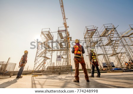 Construction engineers supervising progress of construction project stand on new concrete floor top roof and crane background
