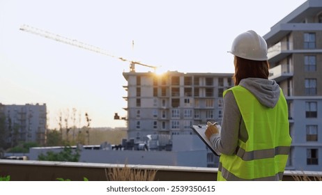 Construction female engineer taking notes and writing on clipboard while inspecting a building site - Powered by Shutterstock