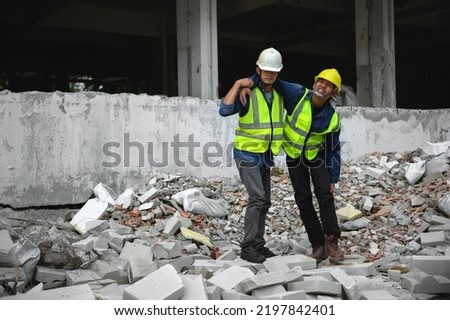 Construction foreman helping to support the body of builder workers stand up on the concrete cement rubble to go first aid room. Knee accident at work