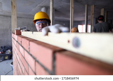 Construction guy helmet measures level brickwork. Level is used when laying bricks in order to check verticality. High quality and stable reading. Indoor use equipment. Smooth brickwork - Shutterstock ID 1718456974