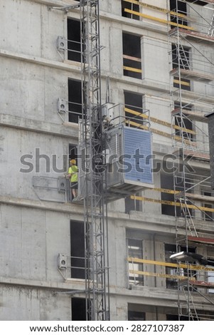 Construction hoist elevator attached to unfinished building facade with workers and scaffolding.