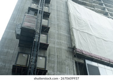 Construction Hoist Elevator on Building Site. Industrial construction hoist elevator attached to an unfinished building. high rise building projects and civil engineering work.