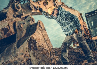 Construction Industry. Heavy Equipment Operator Job. Excavator And Caucasian Worker In Hard Hat. Men Looking Inside Excavator Bucket.