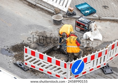 Construction and installation works. Workers using an electric hammer drill and a gasoline generator are repairing a sewer well located on a city road.