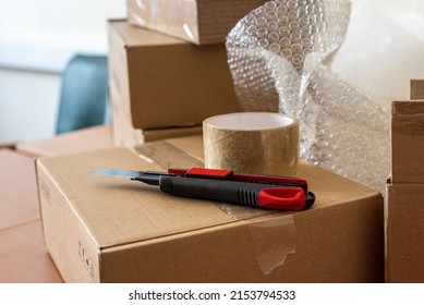 Construction Knife And Sticky Transparent Tape On The Packing Box On The Desk In The Dispatch Office