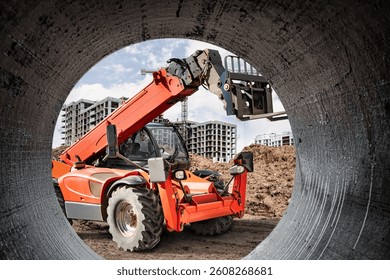 A construction loader is positioned to lift a large pipe at a busy construction site, surrounded by building structures under development in clear weather.